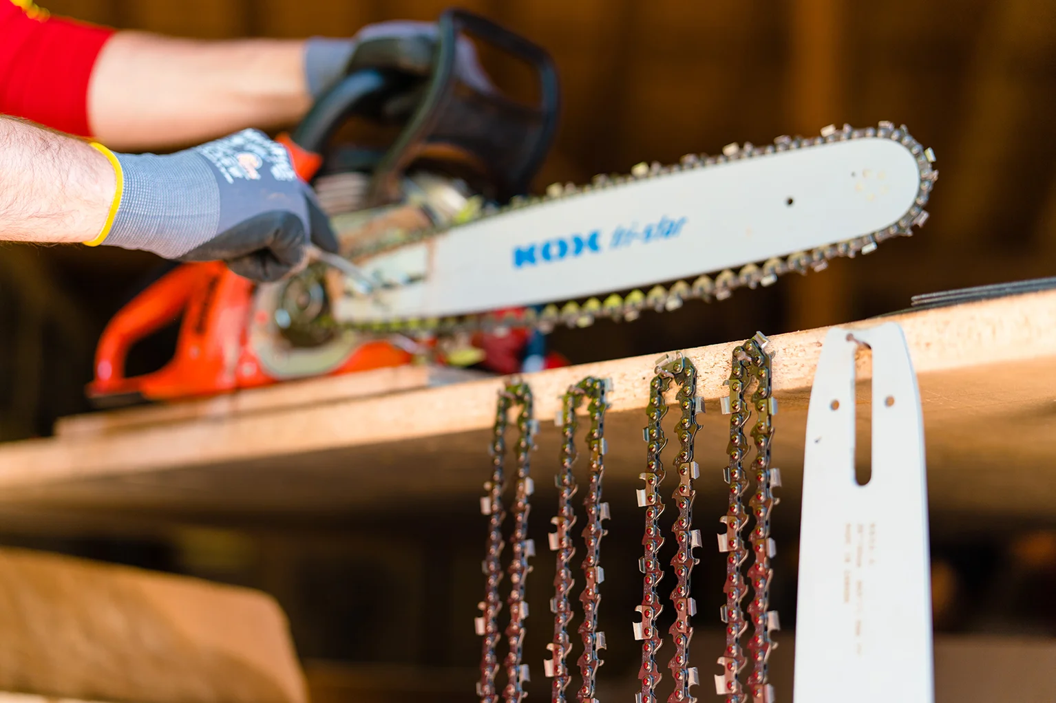 Person mit Handschuhen beim Spannen einer KOX Sgekette an einer Motorsge, im Vordergrund hngen weitere Sgeketten und eine Fhrungsschiene griffbereit an einem Regal.