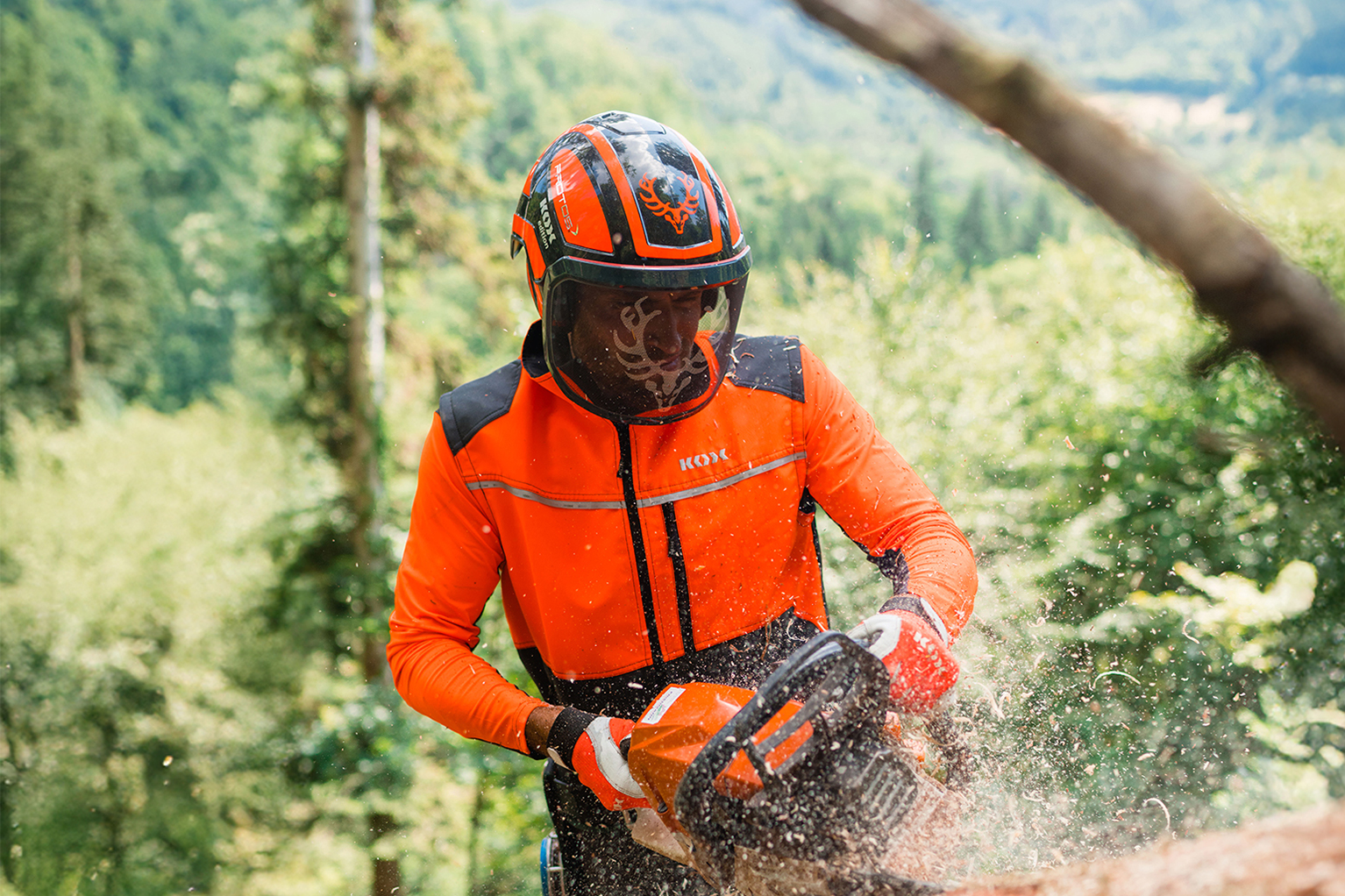 Ein Forstarbeiter in orangefarbener Schutzkleidung zers�gt mit einer Motors�ge einen liegenden Baumstamm.